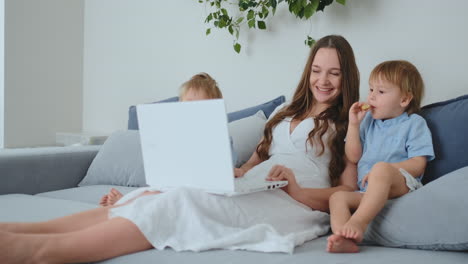 Beautiful-young-mom-and-two-little-kids-boys-are-looking-at-the-laptop-screen-family-photos.-And-they-do-online-shopping.-Call-grandmother-through-video-chat.-Children-show-their-fingers-on-the-laptop-screen-favorite-toys